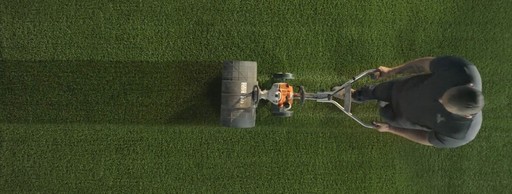 Pictured from above, a man uses a power broom to maintain the appearance of synthetic grass.