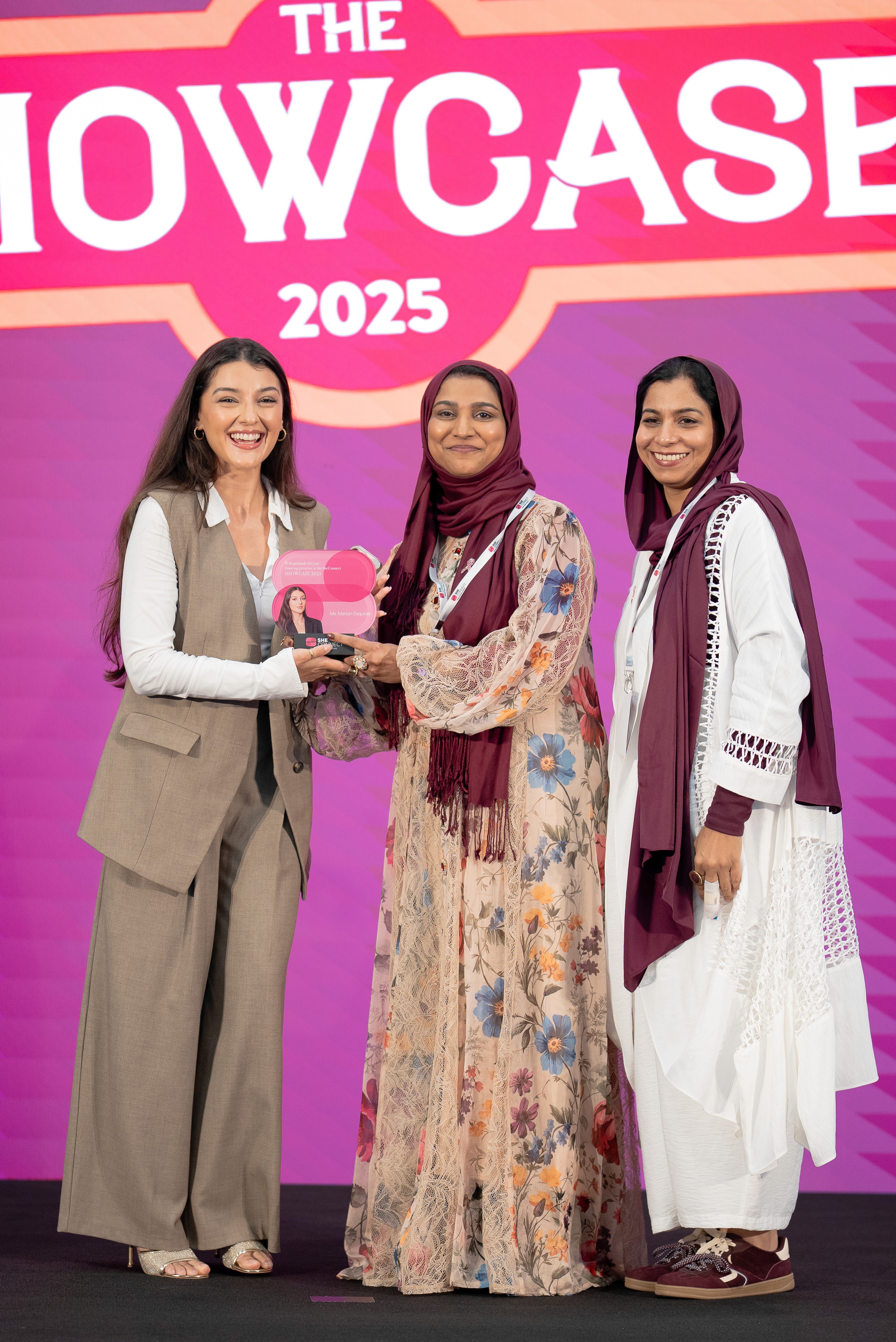 A smiling young man with crossed arms, wearing a plaid shirt and white t-shirt, poses against a dark background.