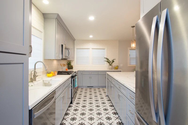 Rustic farmhouse kitchen galley with decorative printed floor tile, blue/grey cabinetry and quartz countertops. Photo by Chris Darnall.