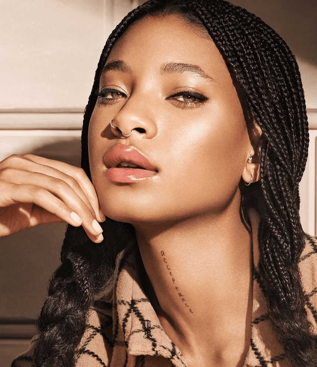 Willow Smith with braided hair, glossy nude lips, and radiant skin, posing in natural light for Dior Beauty.