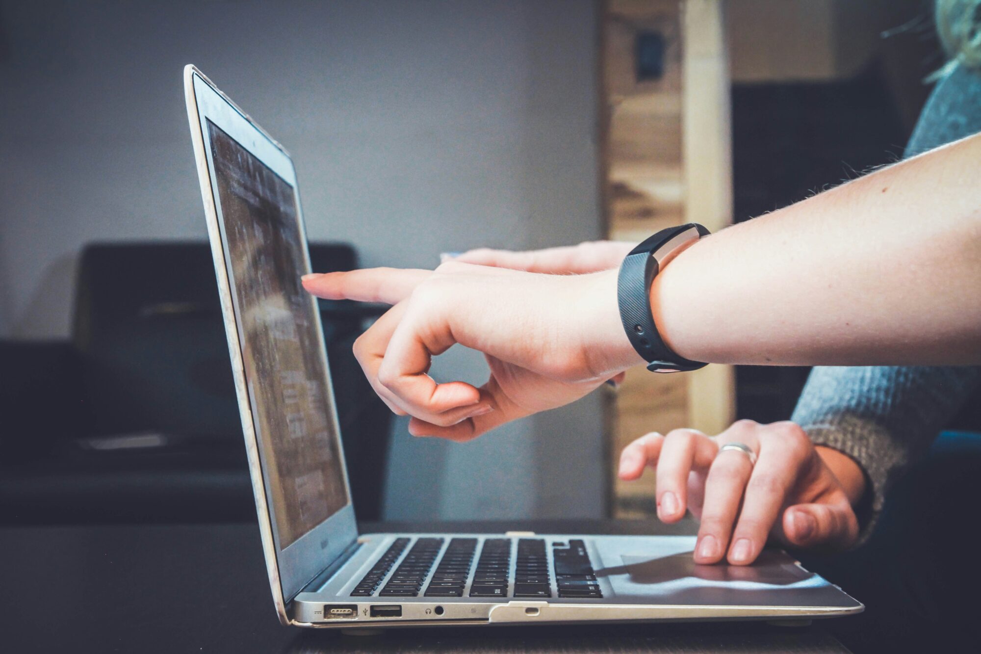 A person's hand pointing at a laptop screen while the other hand is typing on the keyboard.