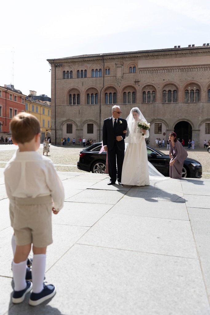 Bambino guarda gli sposi arrivare in piazza, cerimonia di matrimonio a Parma con palazzo storico sullo sfondo