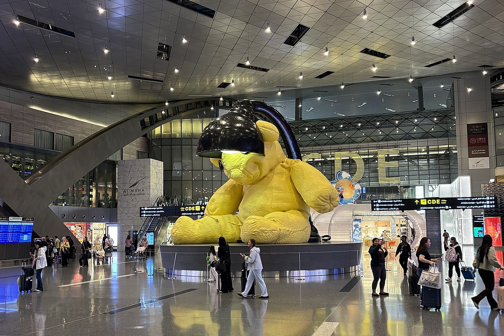 Le Lamp Bear, l'ours jaune géant du hall de l'aéroport Hamad, à Doha, sous la verrière et entouré de voyageurs : l'aéroport élu meilleur du monde en 2021, 2022 et 2024, à 20 minutes de chez moi