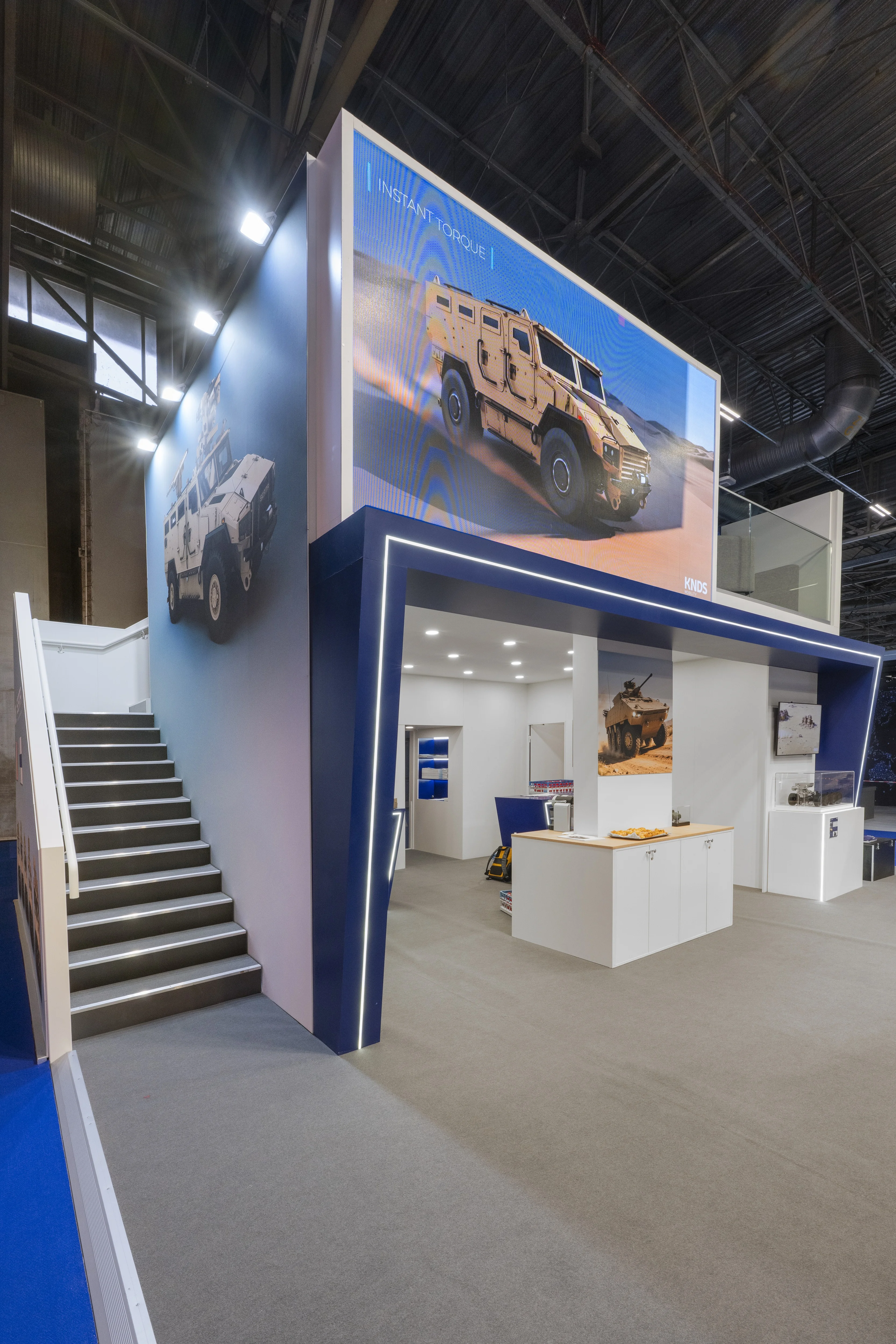 Stand KNDS Mobility conçu et réalisé par Expace à Eurosatory 2026 – espace sur-mesure défense avec blindé SCATA, châssis Celeris écorché, bandeau suspendu « Driving Innovation for Mobility » et lounge à l'étage.