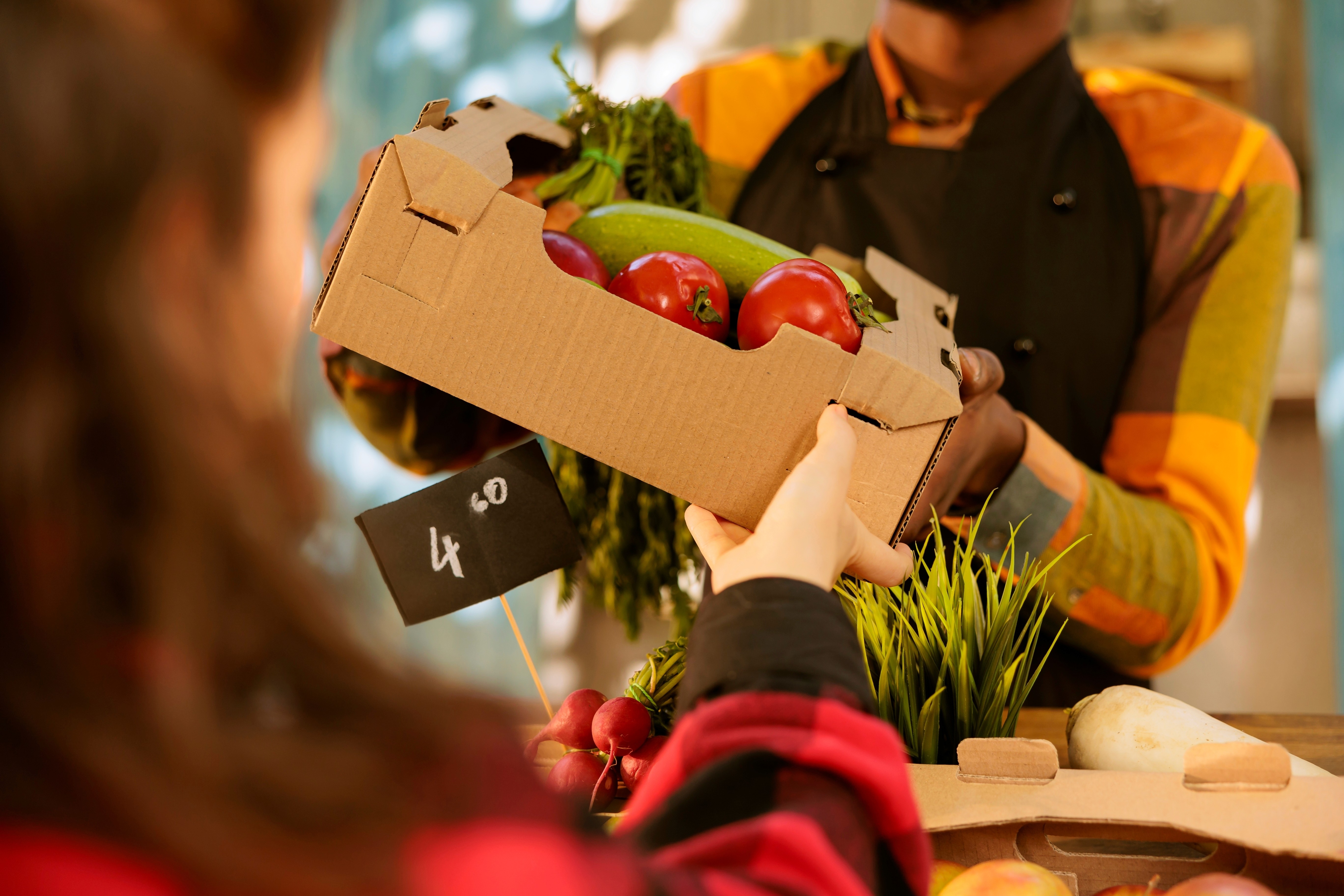 A market trader handing over a small box of vegetables to a customer. Close-up shot.