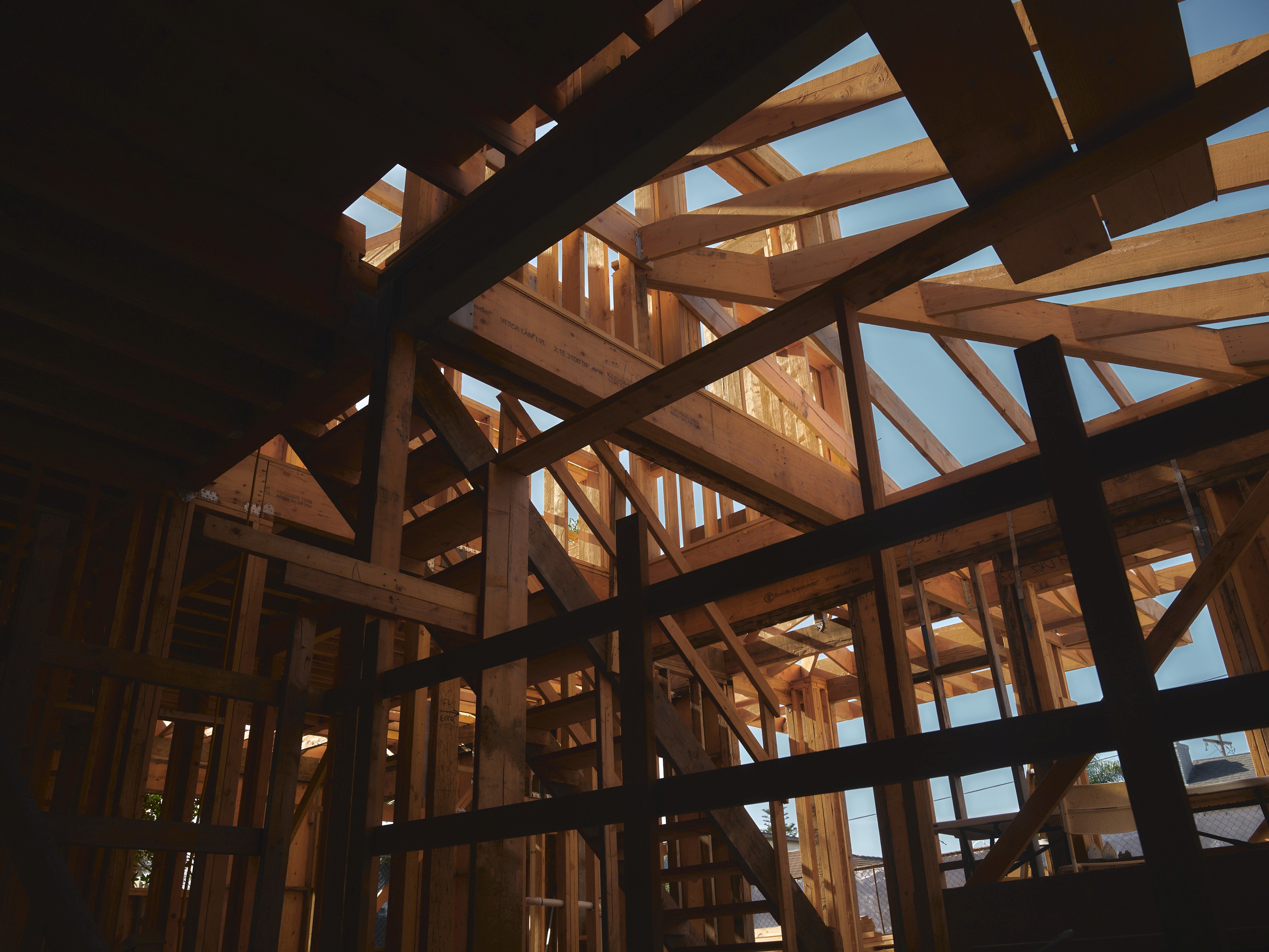 Low-angle shot showing intricate timber roof trusses, wall studs, and floor joists in a rough-framed residential structure
