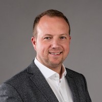 Portrait of a woman with glasses and shoulder-length black hair, green top, smiling.