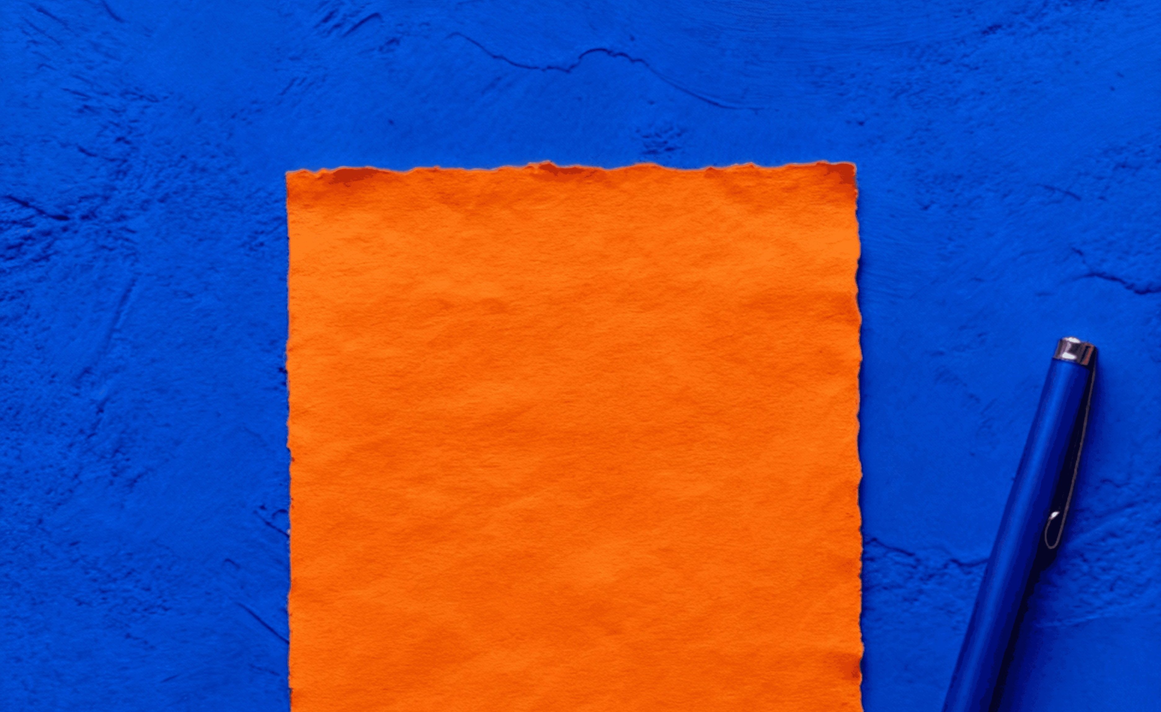Orange torn-edge paper and blue pen placed on a textured blue surface.