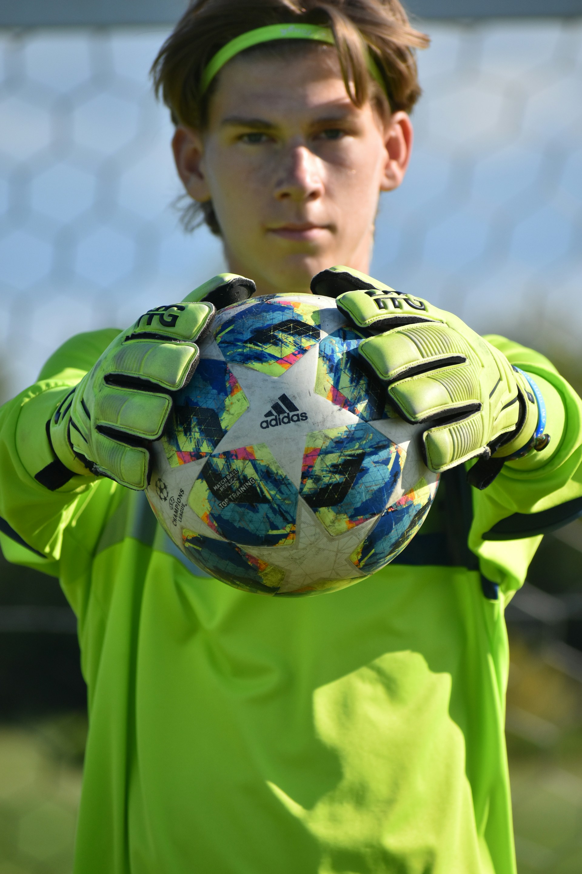 A young soccer goalkeeper in a neon green jersey holding a star-patterned ball with gloved hands.