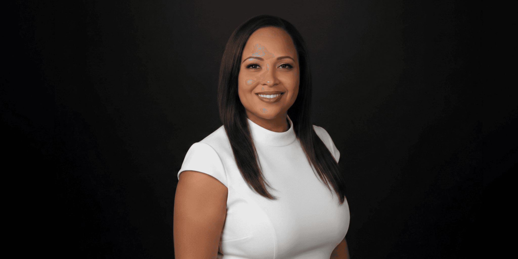 Professional portrait of smiling woman in white top against dark background.
