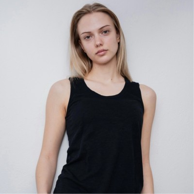 A focused woman with long red hair is seated at a desk, wearing a black blazer and dark blouse. She intently looks at camera, smiling slightly, with an open laptop in front of her. The setting is a warm and serene office setup in the background. Soft daylight filters through, creating a calm atmosphere. The composition captures her in a frontal profile with a clear emphasis on her concentration and the serene indoor setting.