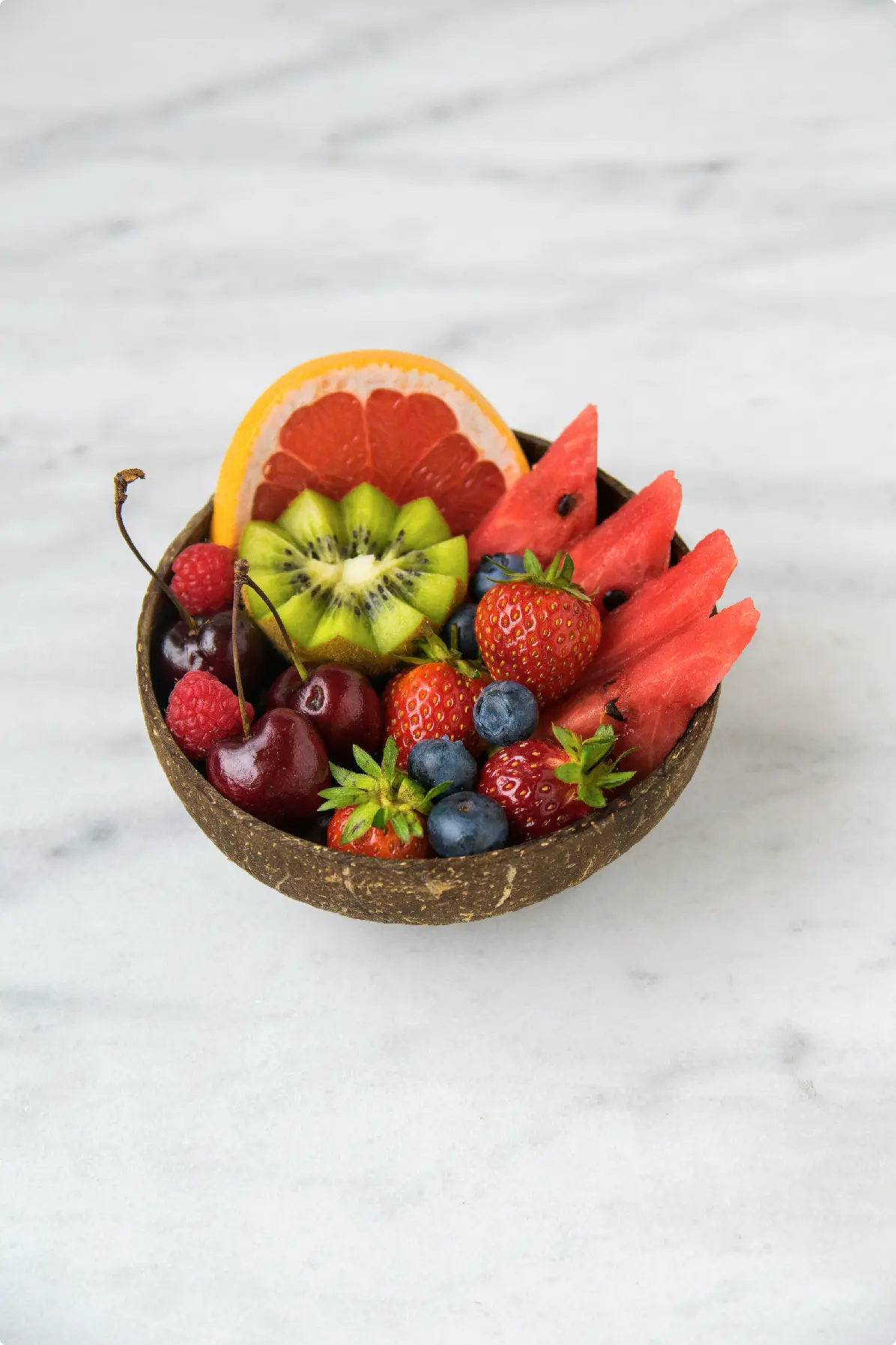A colorful bowl filled with various fruits and edible flowers arranged beautifully on a light background.