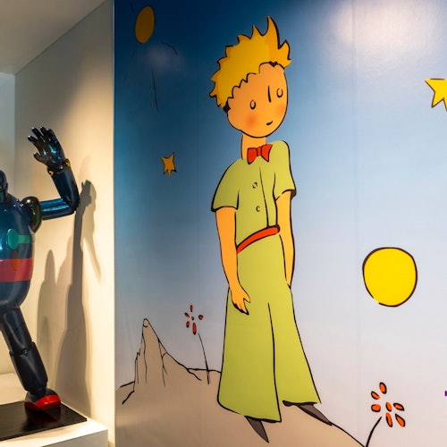 A wall mural of "The Little Prince" next to a robot figurine on a pedestal.