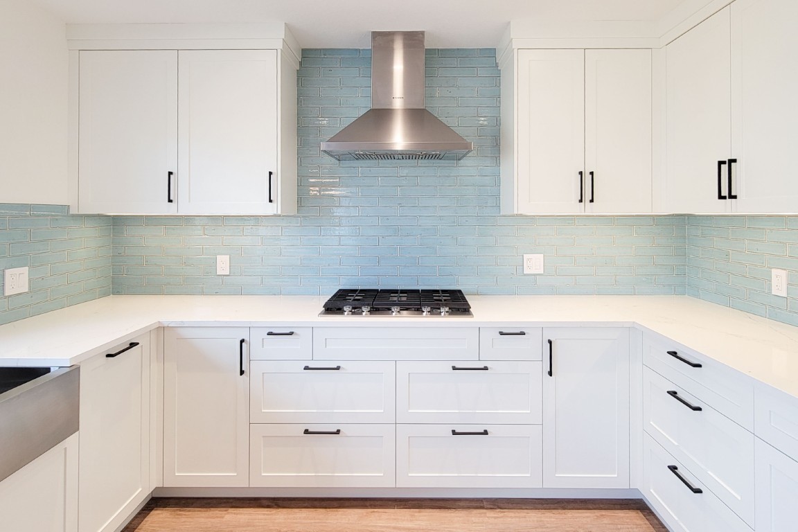 Image of Modern kitchen design with white cabinets, blue tiles, and stainless steel range hood by KHD Homes.