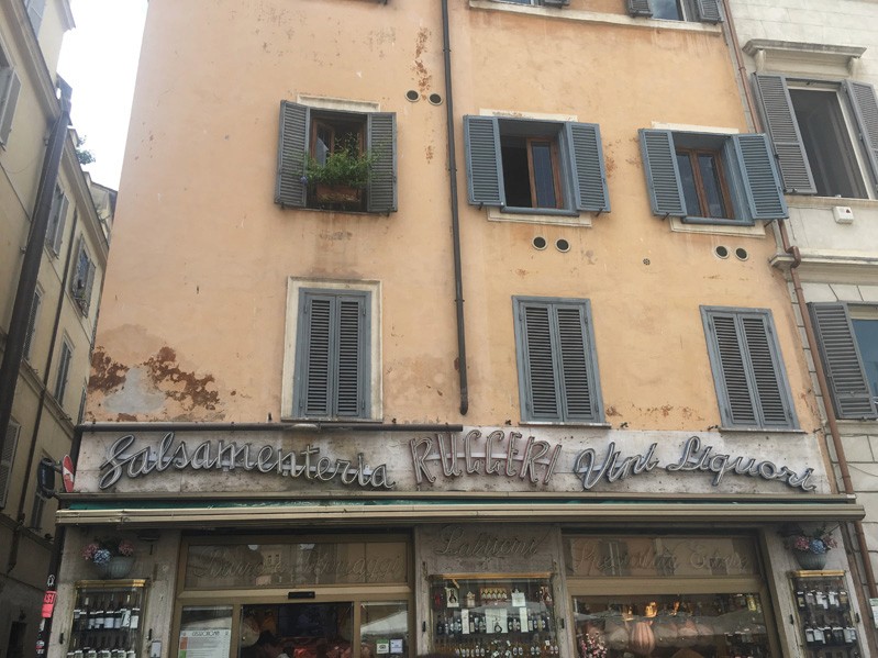 A photo of an old building with window protectors and a shop under them, with some text logo.