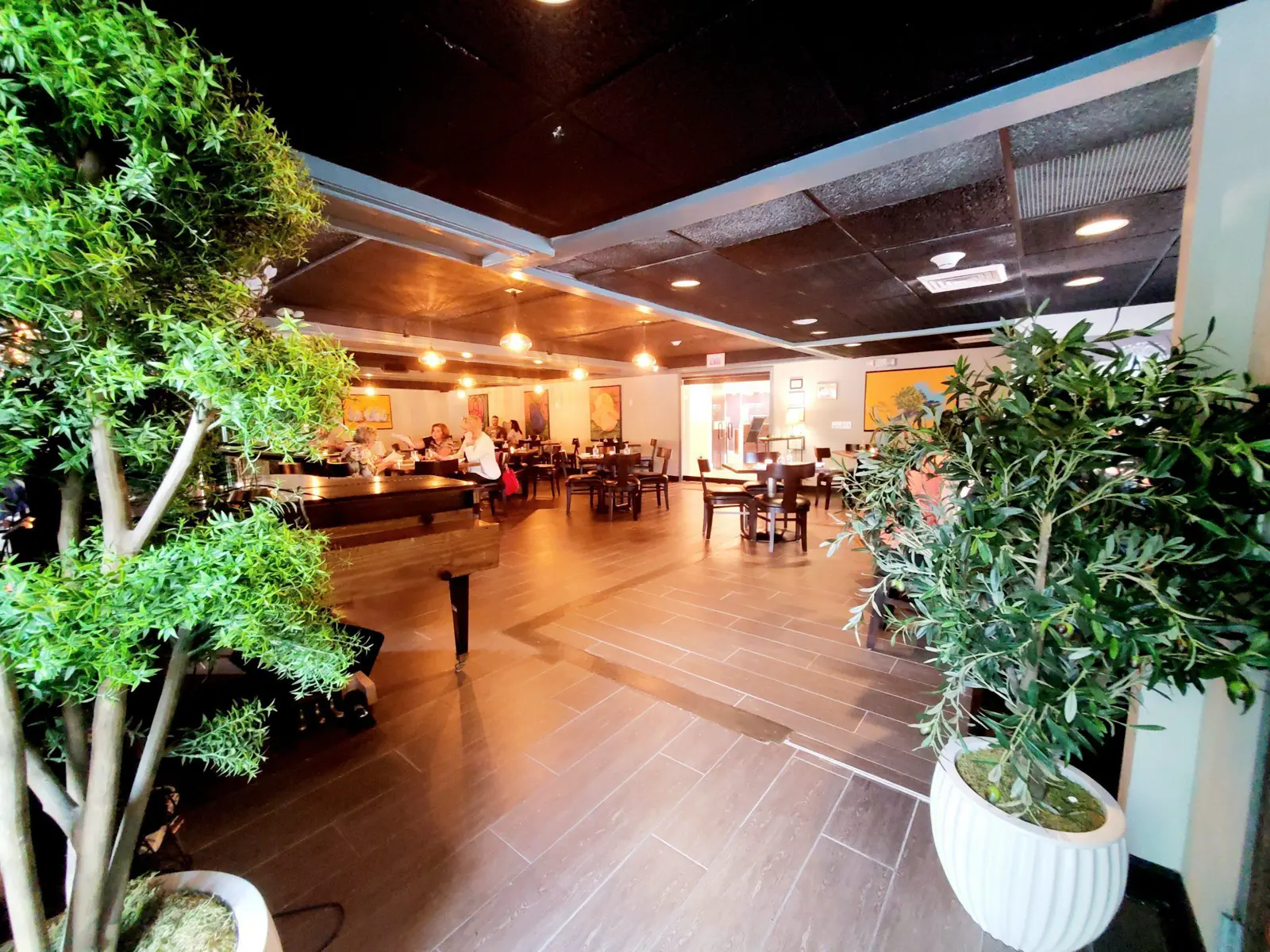 A restaurant interior with customers, a piano, and potted trees.