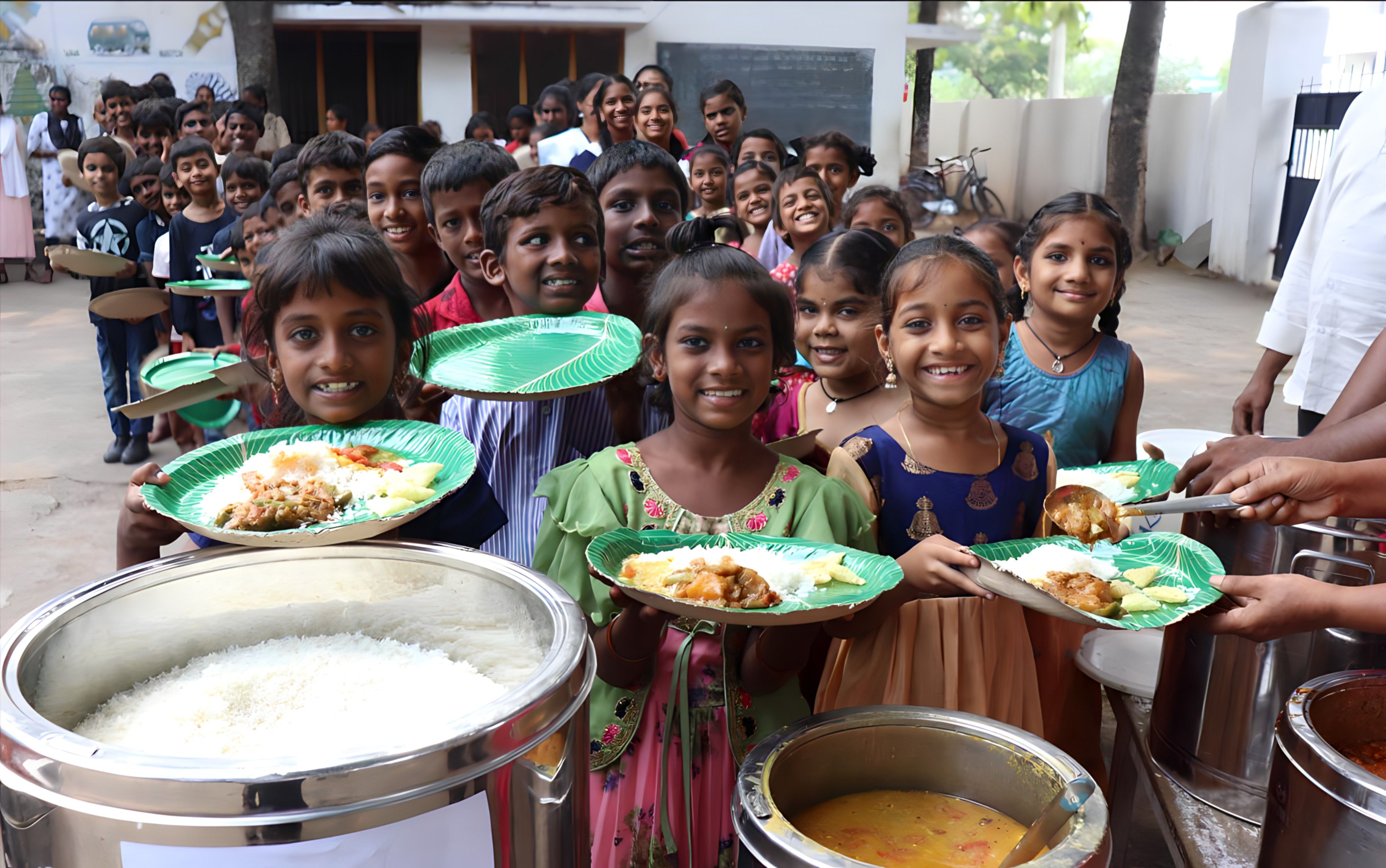Smiling children hold plates of hot food while waiting in line at a meal distribution site.