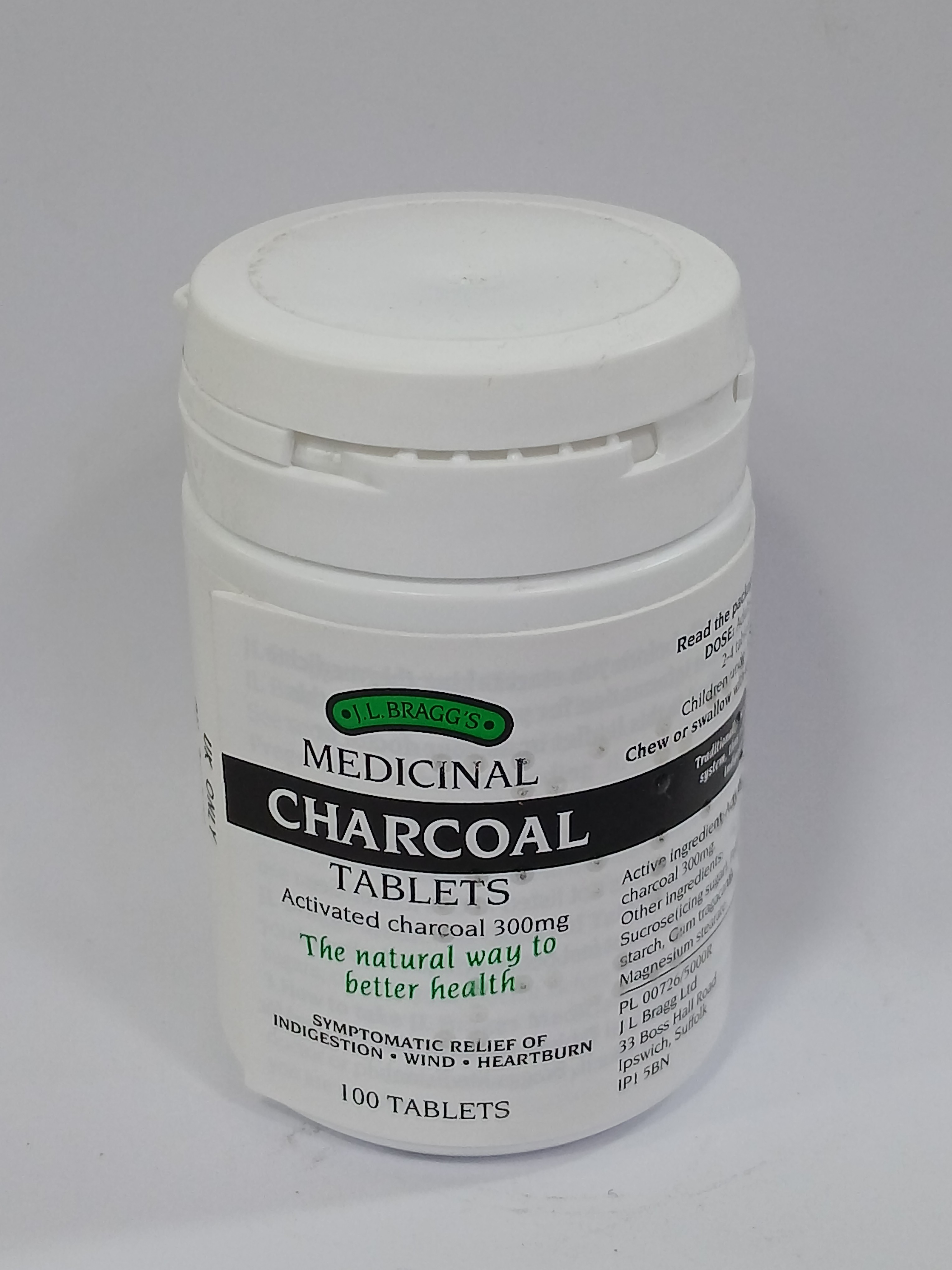 A white plastic jar with a white lid contains 100 greenish-black medicinal tablets, featuring printed text in green and black on the label.