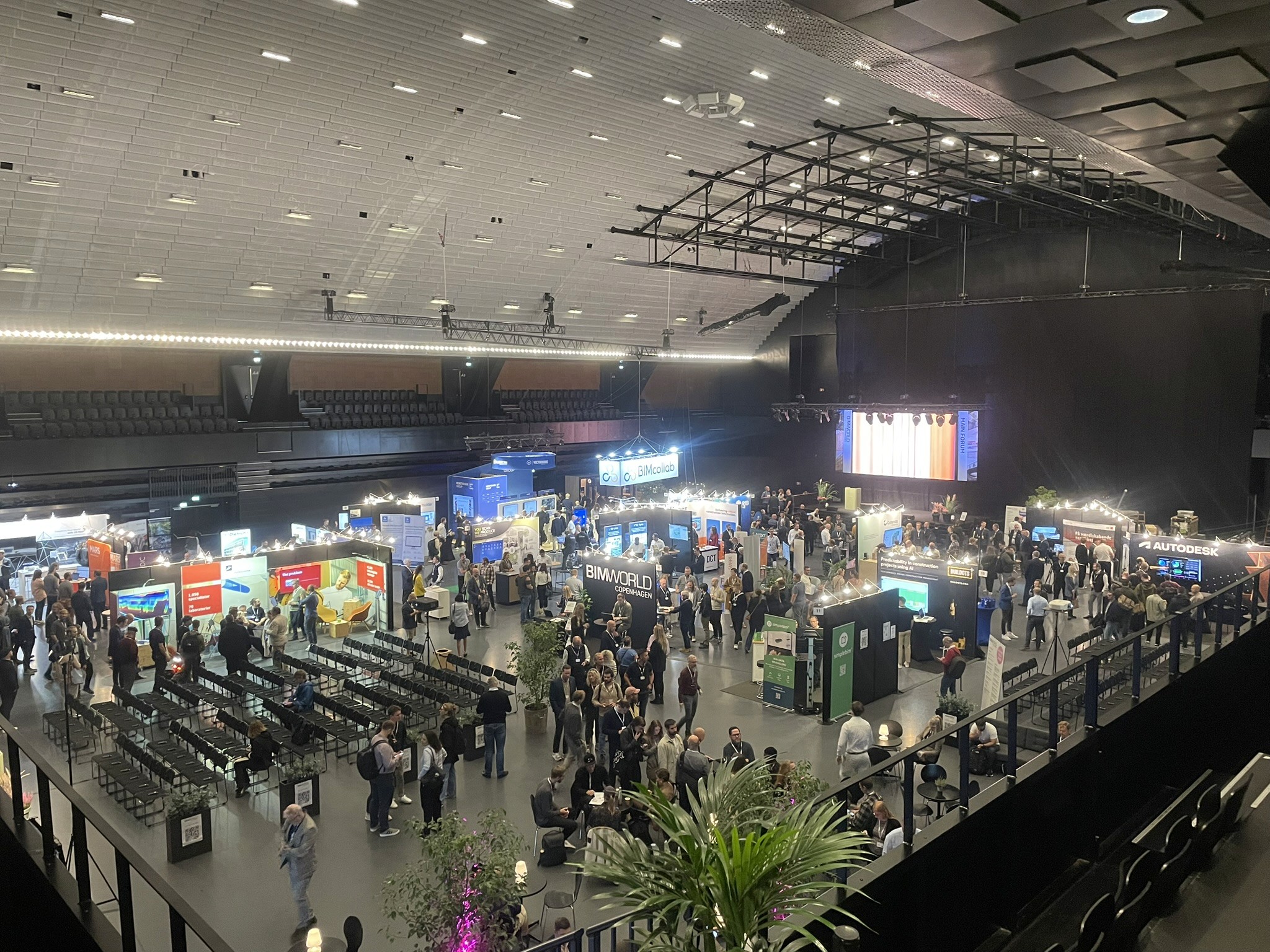 A man stands while two people sit at a table in an office setting, smiling and engaged in conversation. The mood is friendly and collaborative.