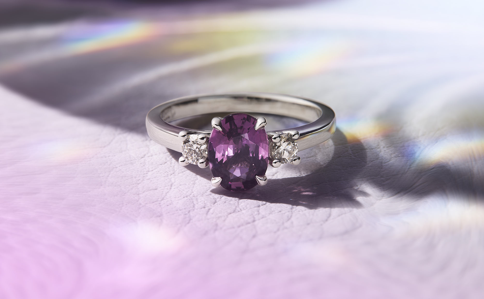 Elegant purple gemstone engagement ring with diamond accents on a light background.