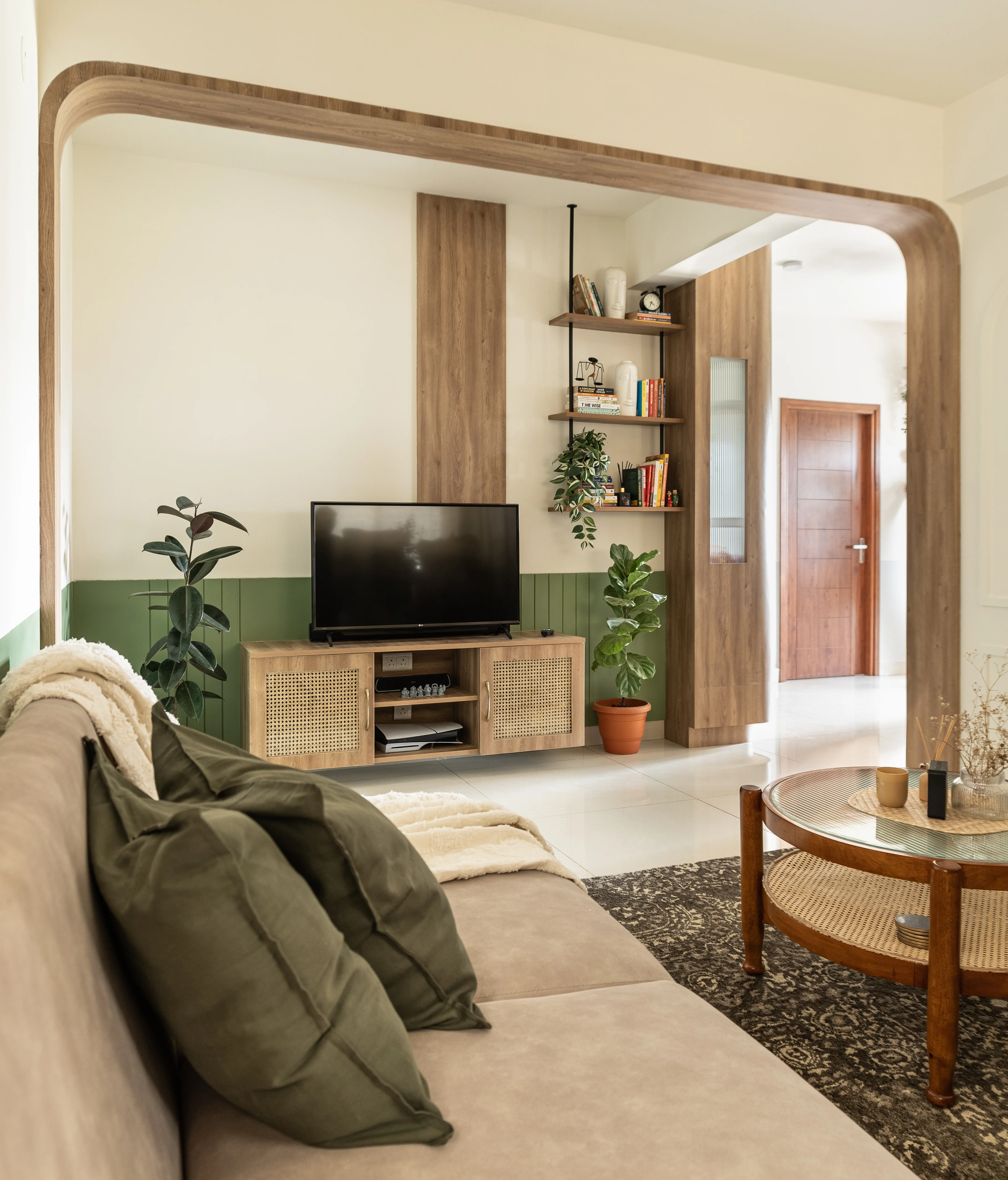 Tropical-themed living room featuring a couch, coffee table, TV, and a plant, framed by an arch and light wood accents