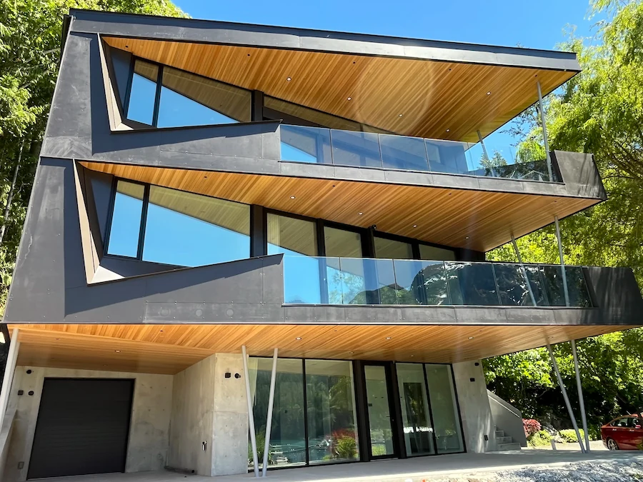Three-storey contemporary home featuring angled architecture and full-height frameless glass balcony railings.