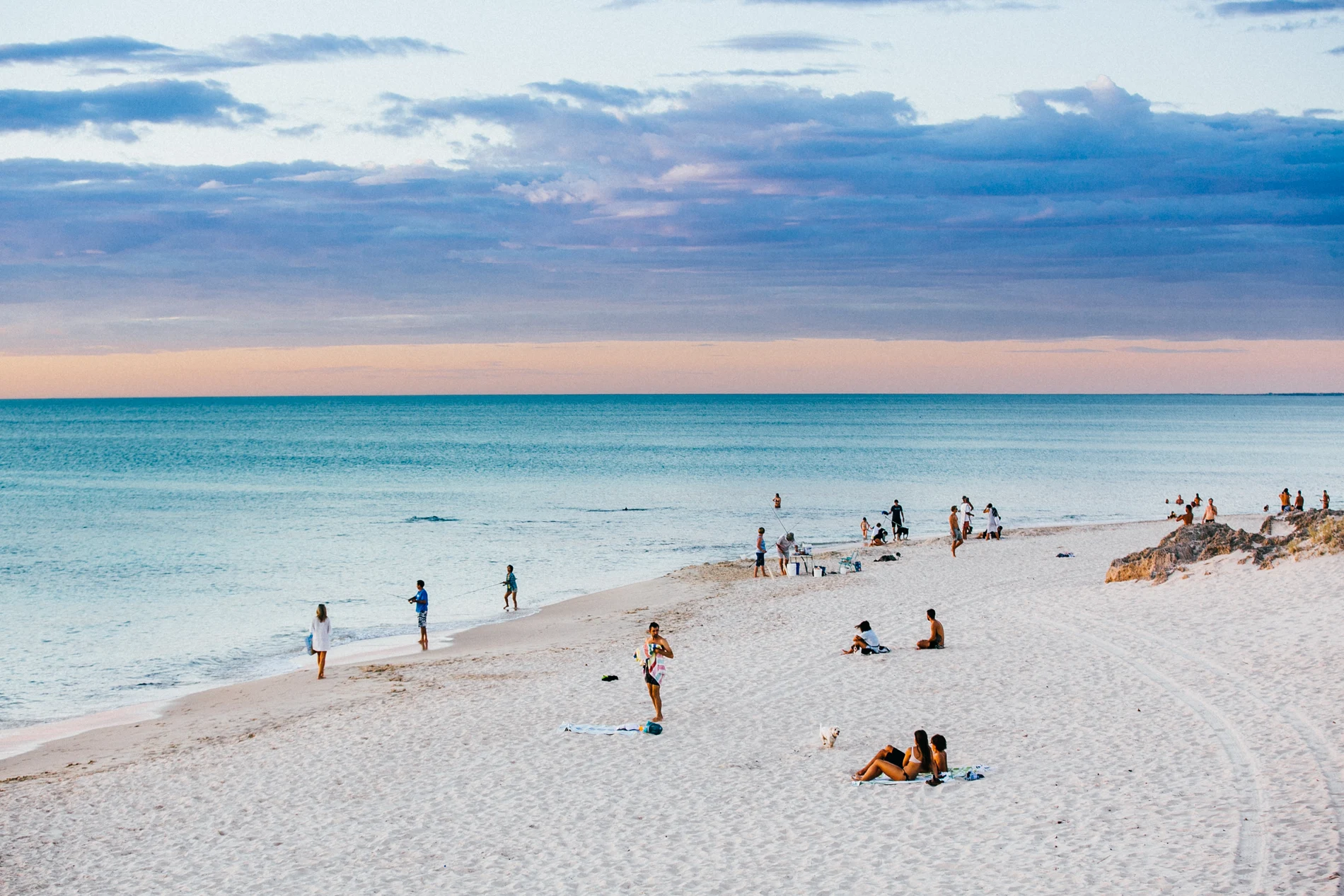 A white sand beach in the late afternoon, groups of people sitting above the turquoise shallows