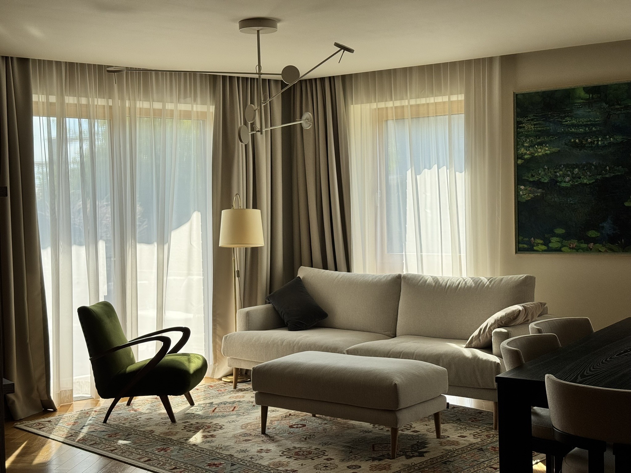 U26 – svetainė su šviesia sofa, žaliu foteliu ir raštuotu kilimu.