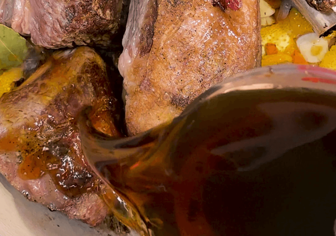 Liquid being poured over short ribs in a pan getting ready to braise