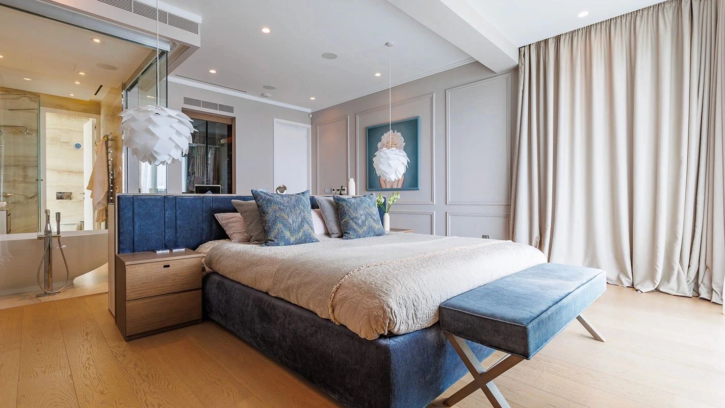 Seafront Residence Limassol master suite with upholstered bed, layered lighting, and glass-partitioned ensuite