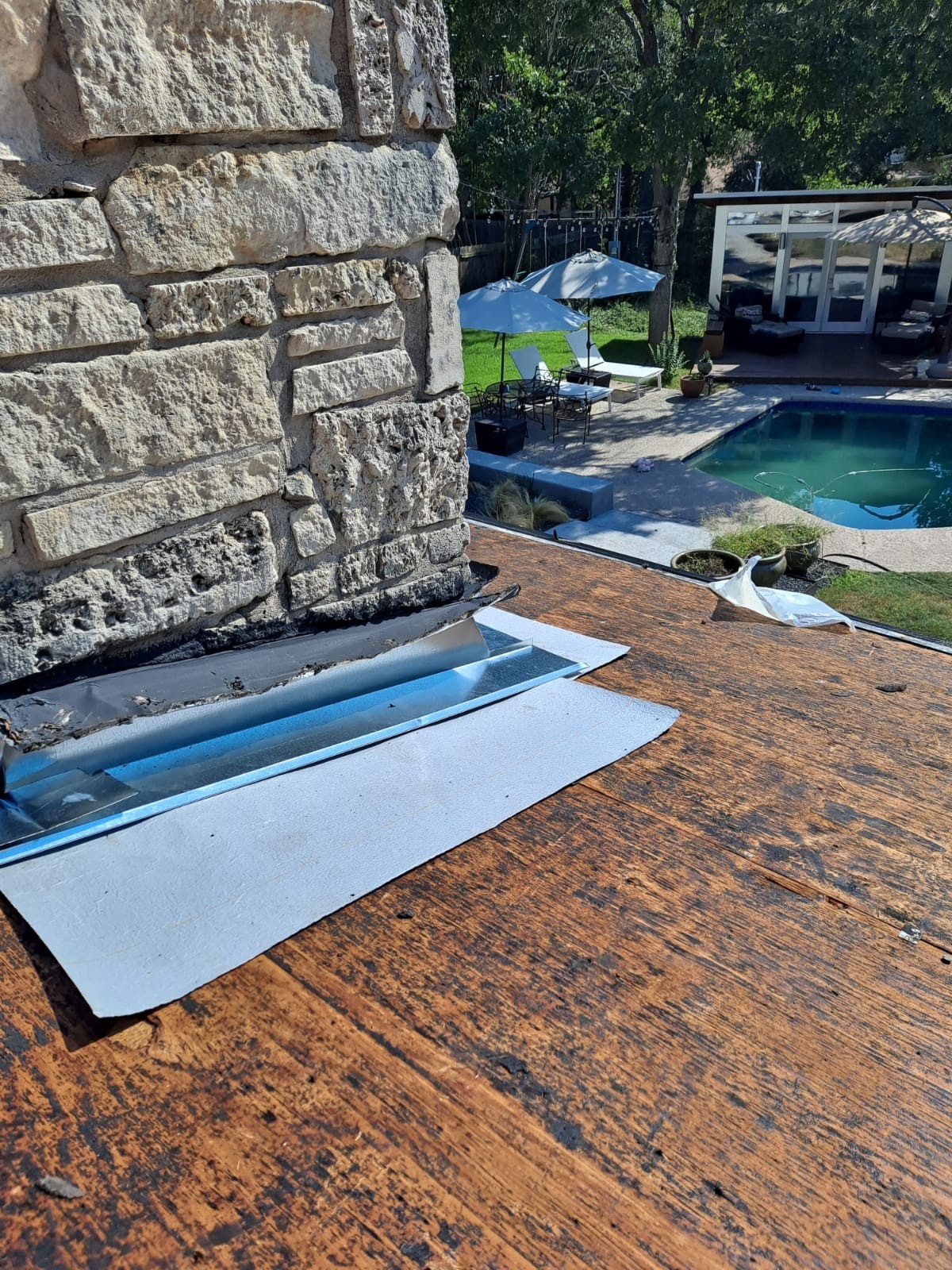 New metal flashing around a stone chimney on exposed roof decking.