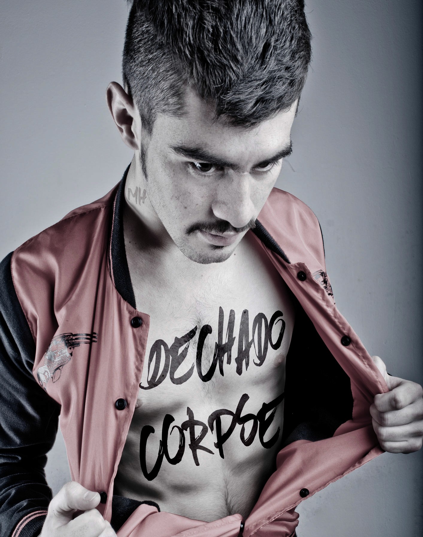 Close-up shot of a man with a mustache opening a red and black bomber jacket to reveal "DECHADO CORPSE" written in bold black ink across his chest.