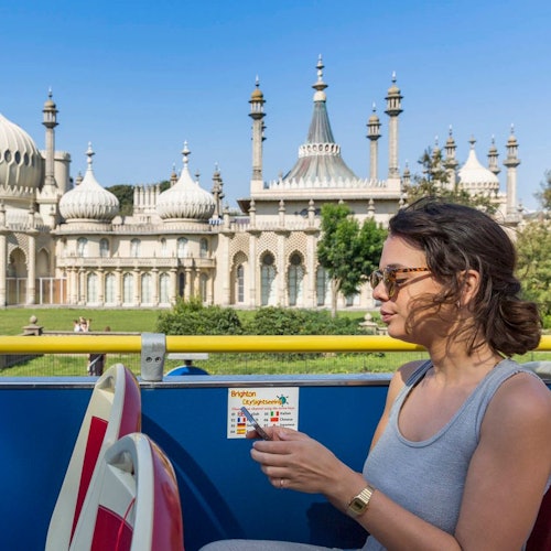 A woman sitting on a bus with the ornate, domed Royal Pavilion building in the background on a sunny day.