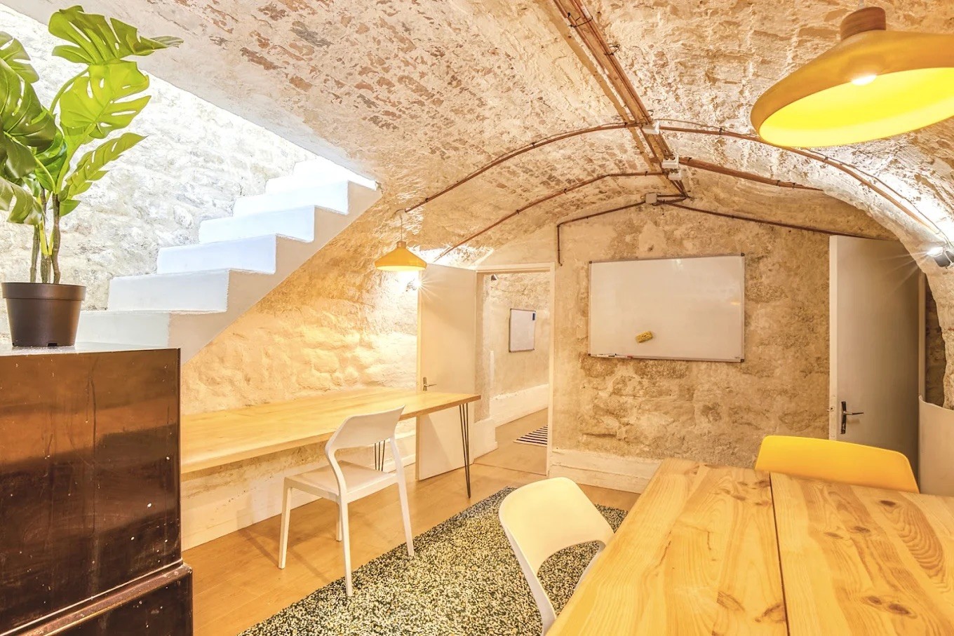 Espace de travail sous voûte en pierre naturelle avec tableau blanc, mobilier de bureau fonctionnel et éclairage doux.