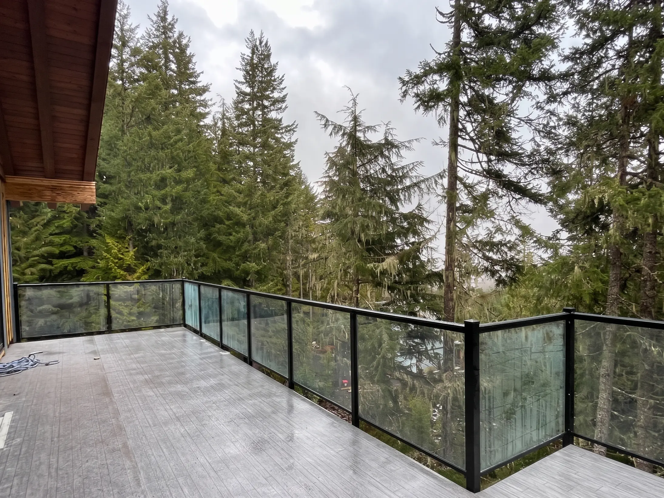 Frameless glass railing on an elevated outdoor deck overlooking dense Pacific Coast evergreen forest
