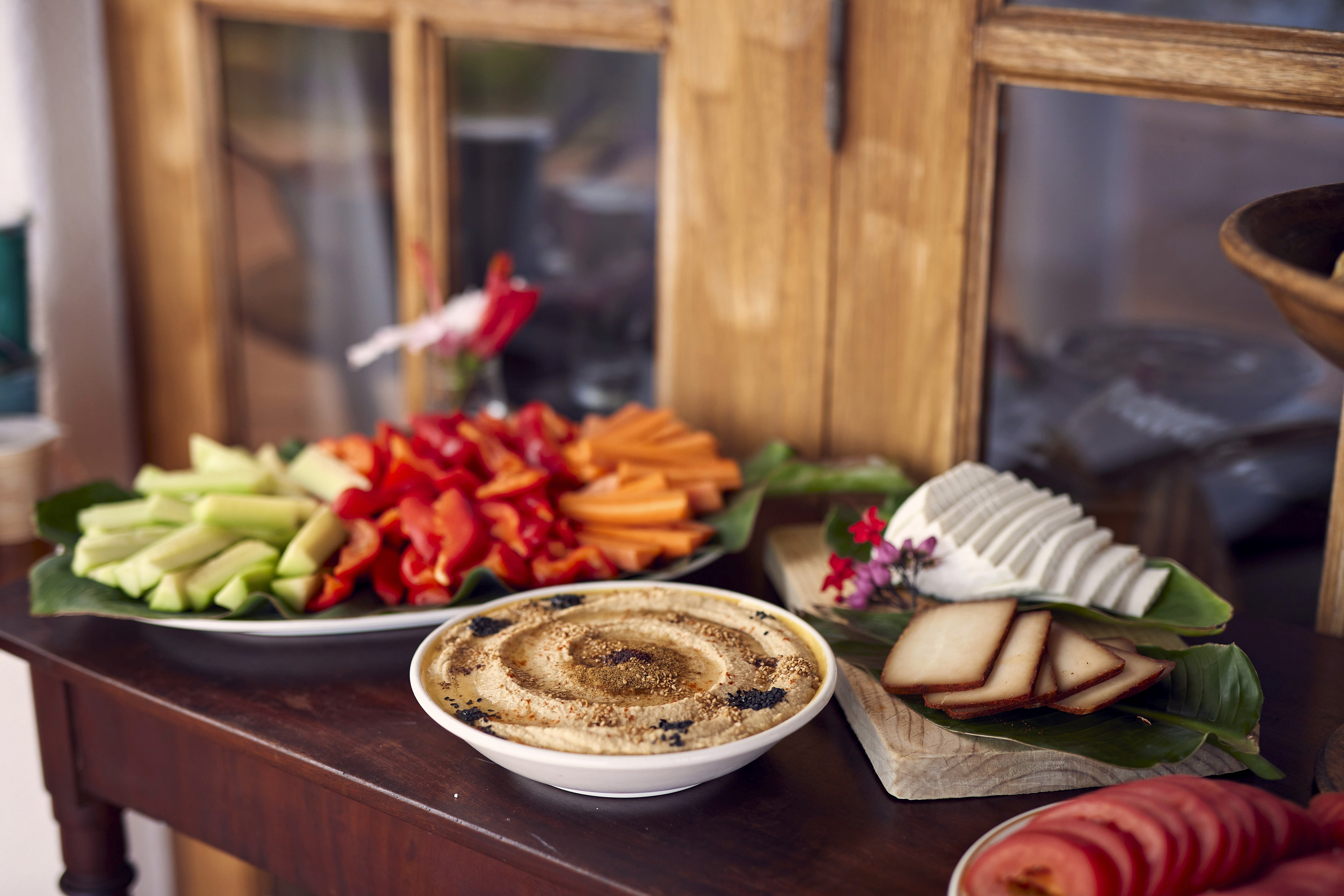 Angerichtetes Buffet mit Gemüsesticks, Paprika, Möhren, Hummus und Käse auf einem Holztisch