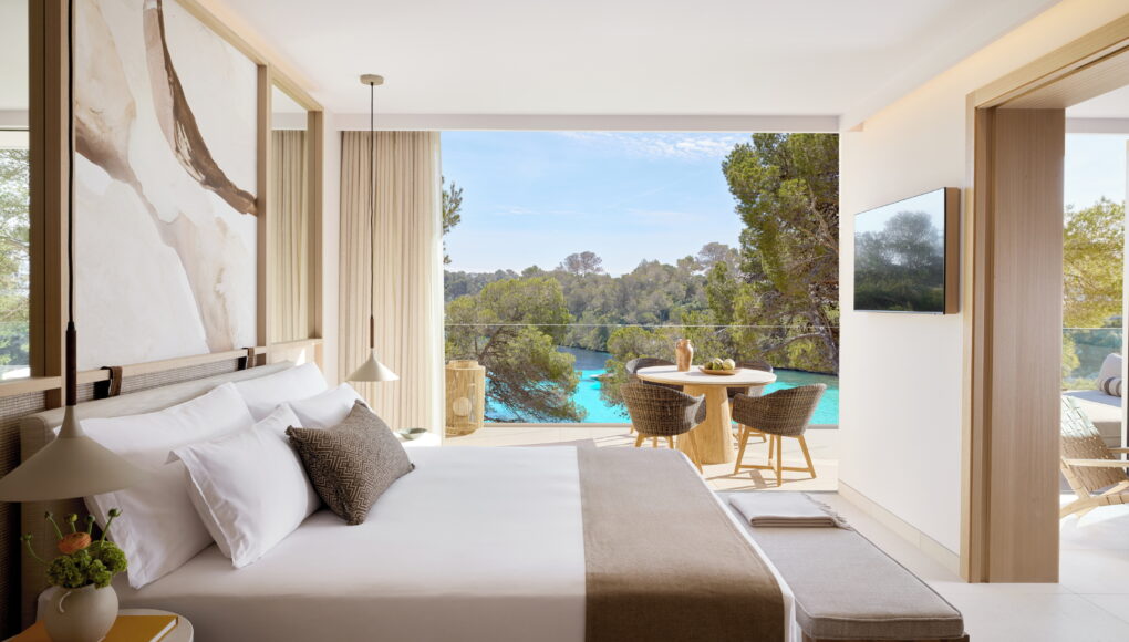 Blick aus einem luxuriösen Schlafzimmer auf einen privaten Balkon mit Sitzgelegenheit und spektakulärer Aussicht auf eine azurblaue Meeresbucht.