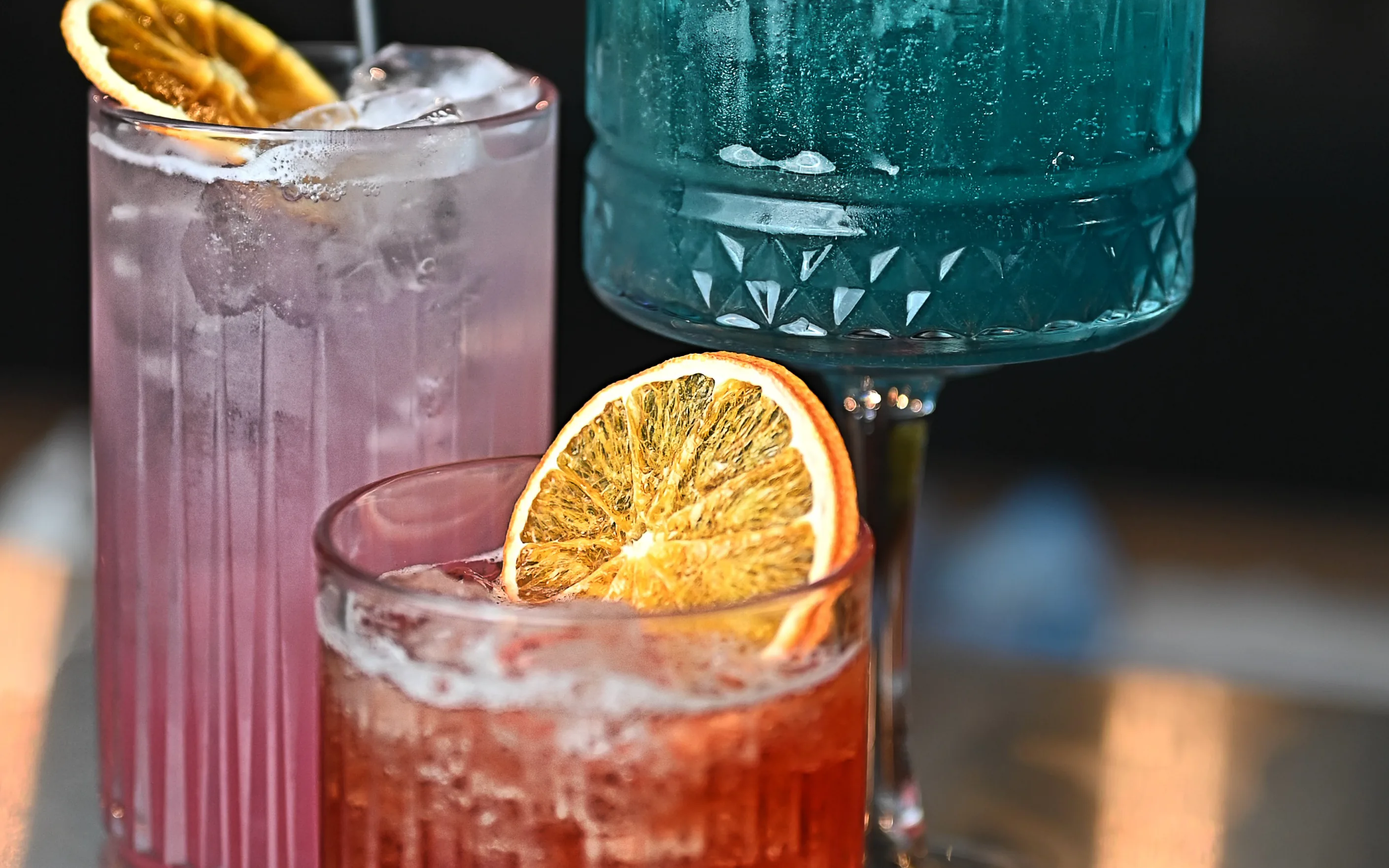 Close-up on a dark background showing a selection of premium cocktails in various glasses, garnished with citrus slices, suggesting exclusive bottle service.