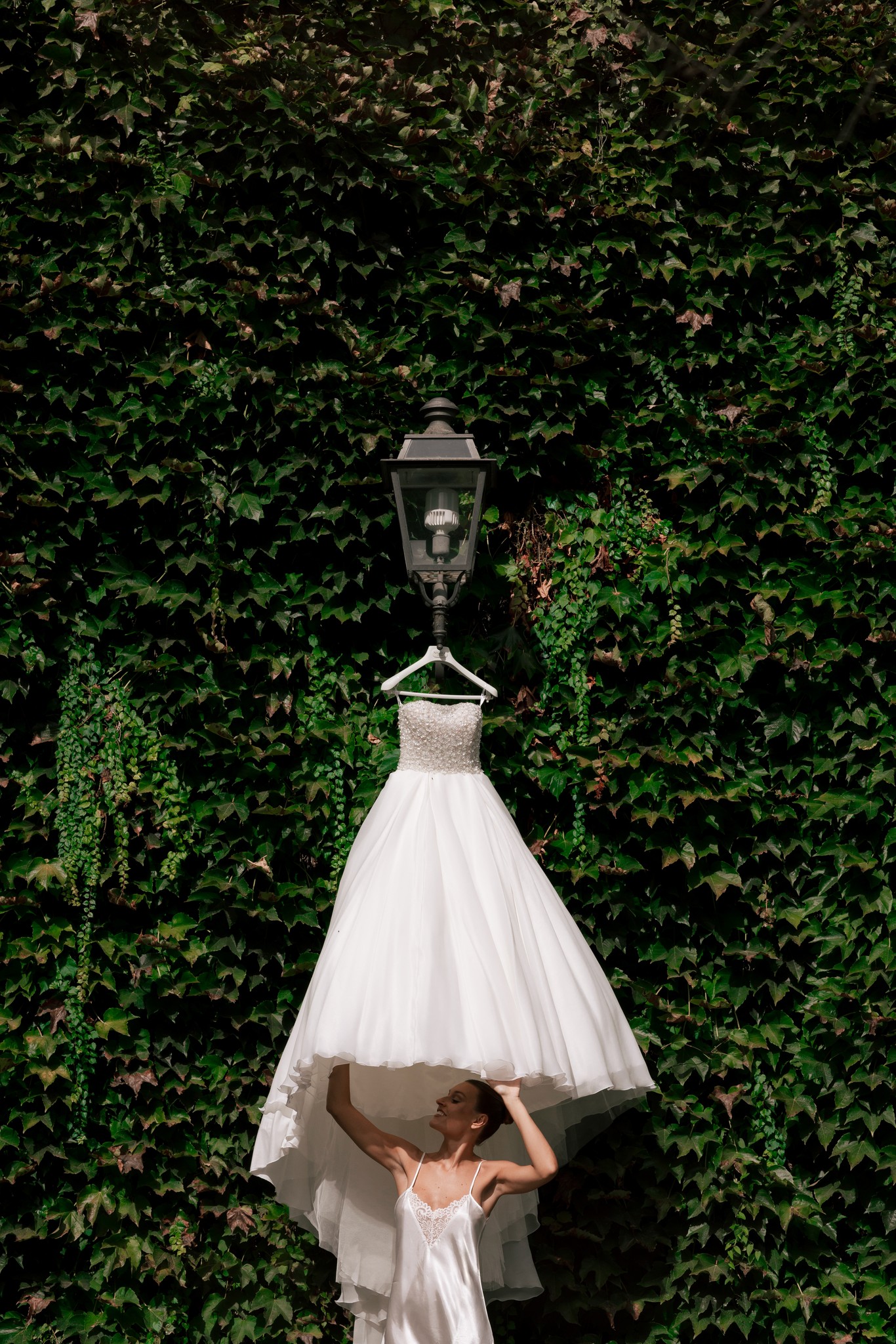 Abito da sposa appeso davanti alla parete d'edera della Villa Ferrari, dettaglio di preparativi matrimoniali