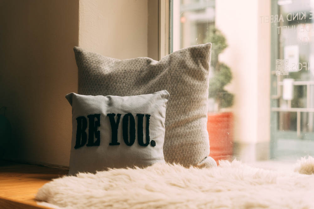 Inspirierendes Detailfoto eines Kissens mit der Aufschrift "BE YOU." auf einer gemütlichen Fensterbank in einem modernen Raum.