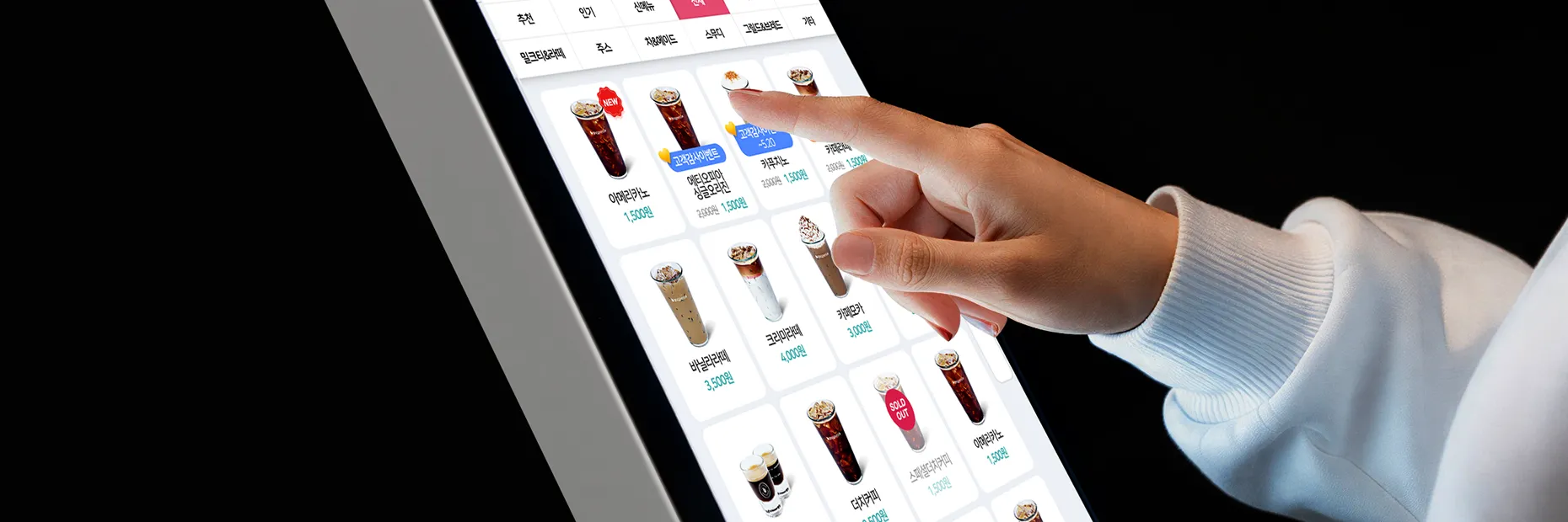 다양한 음료 메뉴가 배열된 키오스크 화면에서 항목을 터치해 선택하는 장면