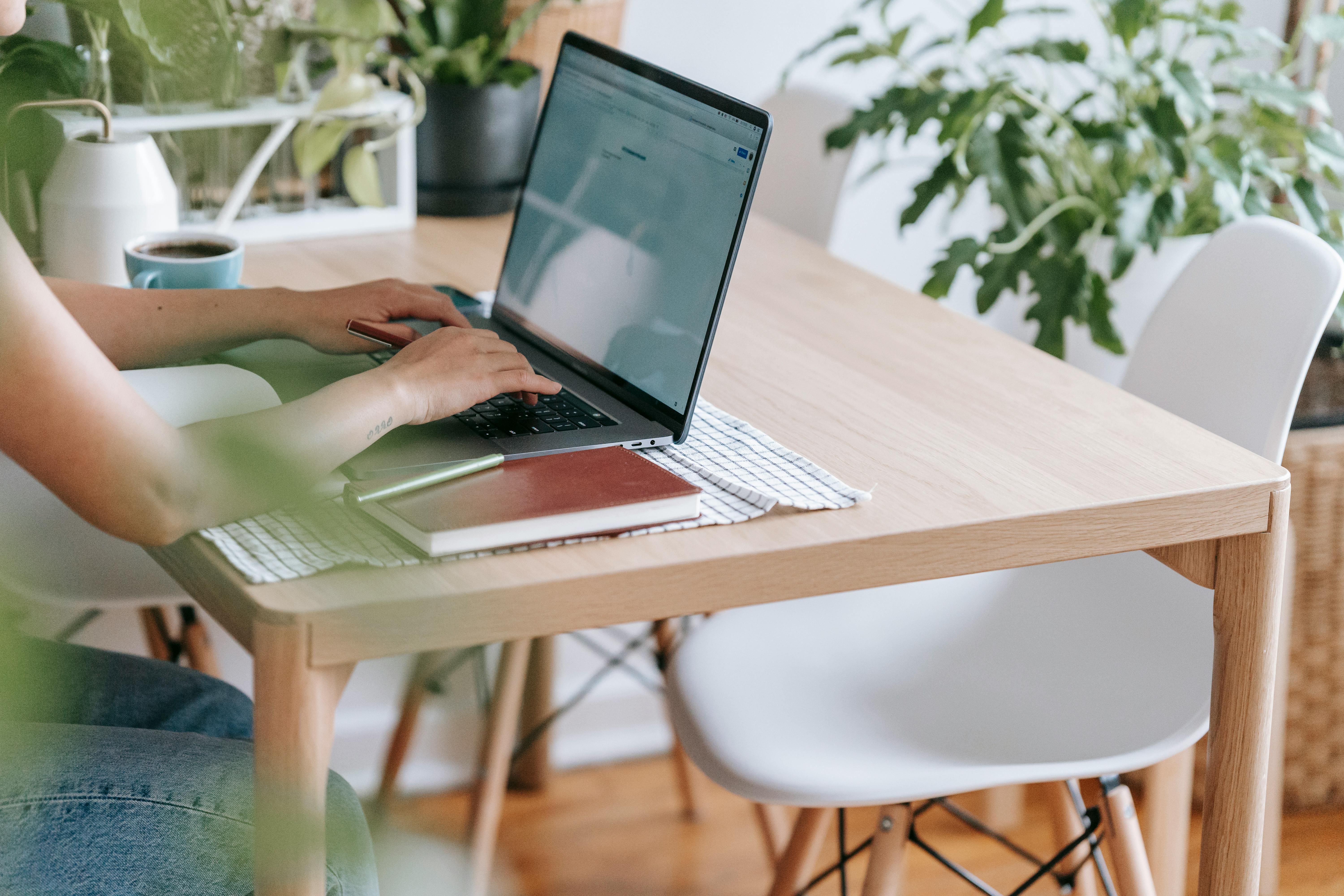 An image of a person at a wooden table, typing on a laptop.