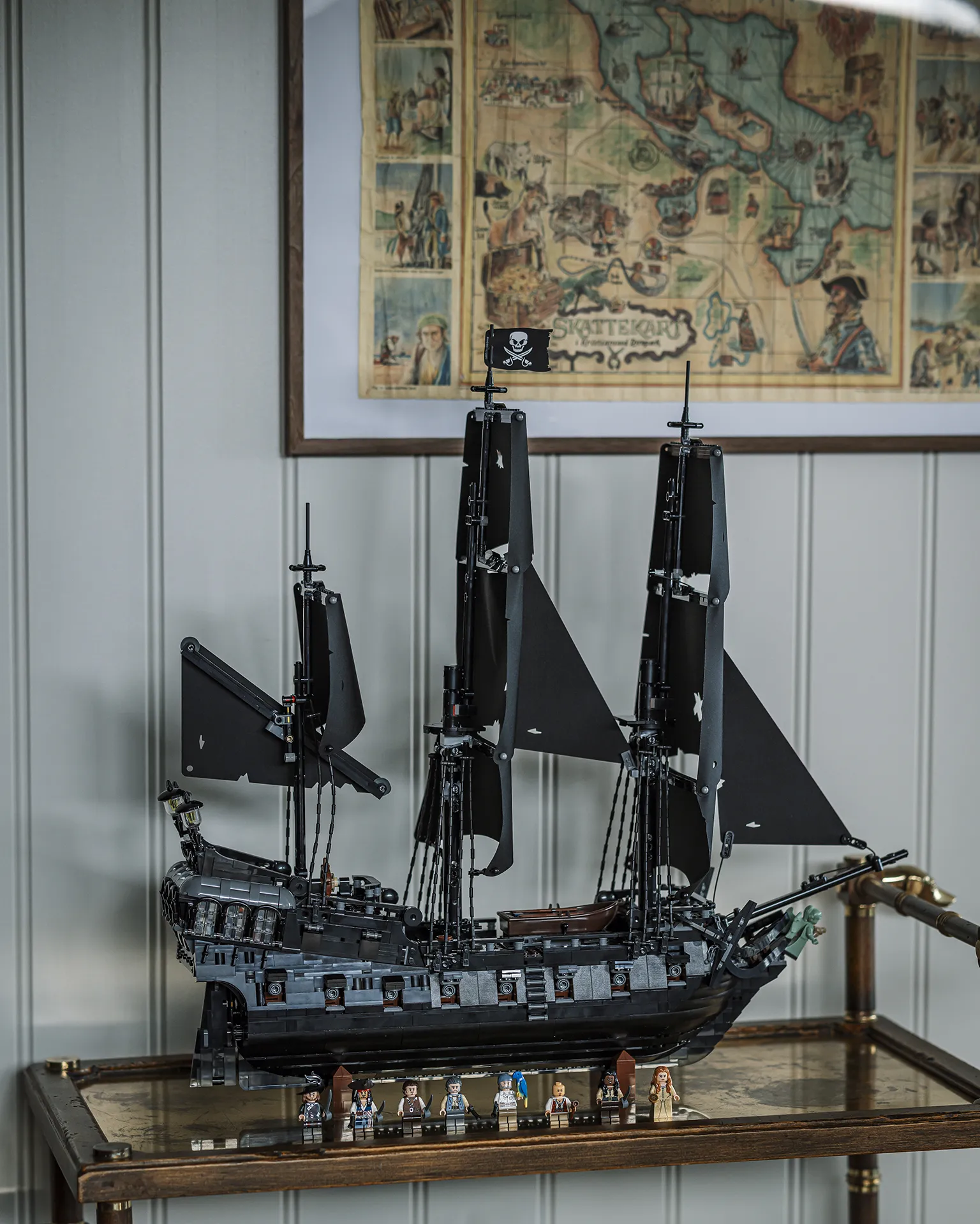 LEGO® modell av "Black Pearl" utstilt på en tralle med et bilde av et skattekart i bakgrunnen