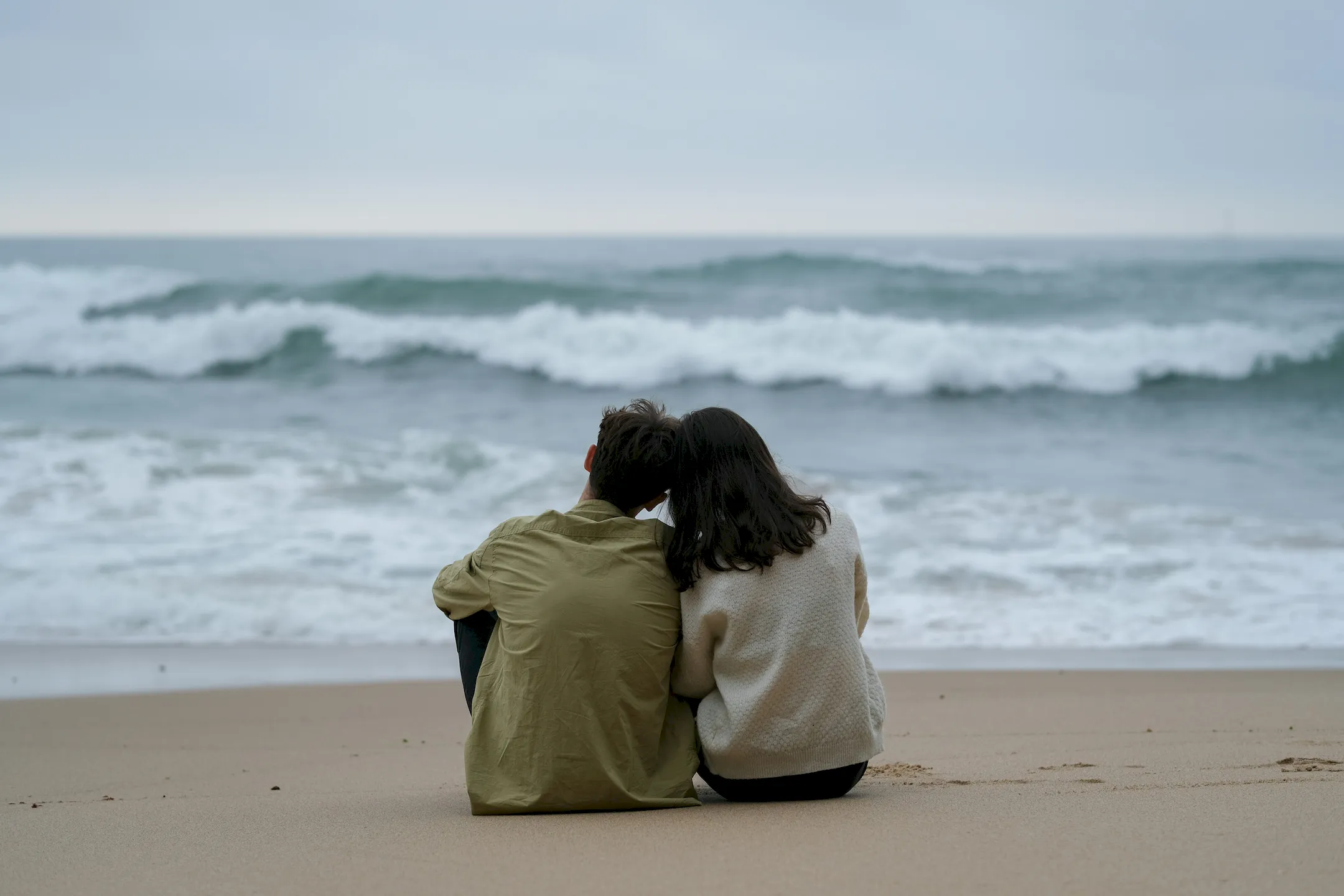 A couple leaning into each other on a beach looking at the waves