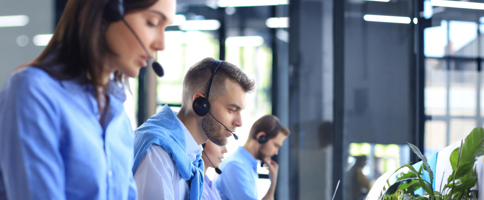 A modern living room with dark walls and furniture, accented with plants and colorful pillows. The room is lit with neon lights, creating a moody atmosphere.