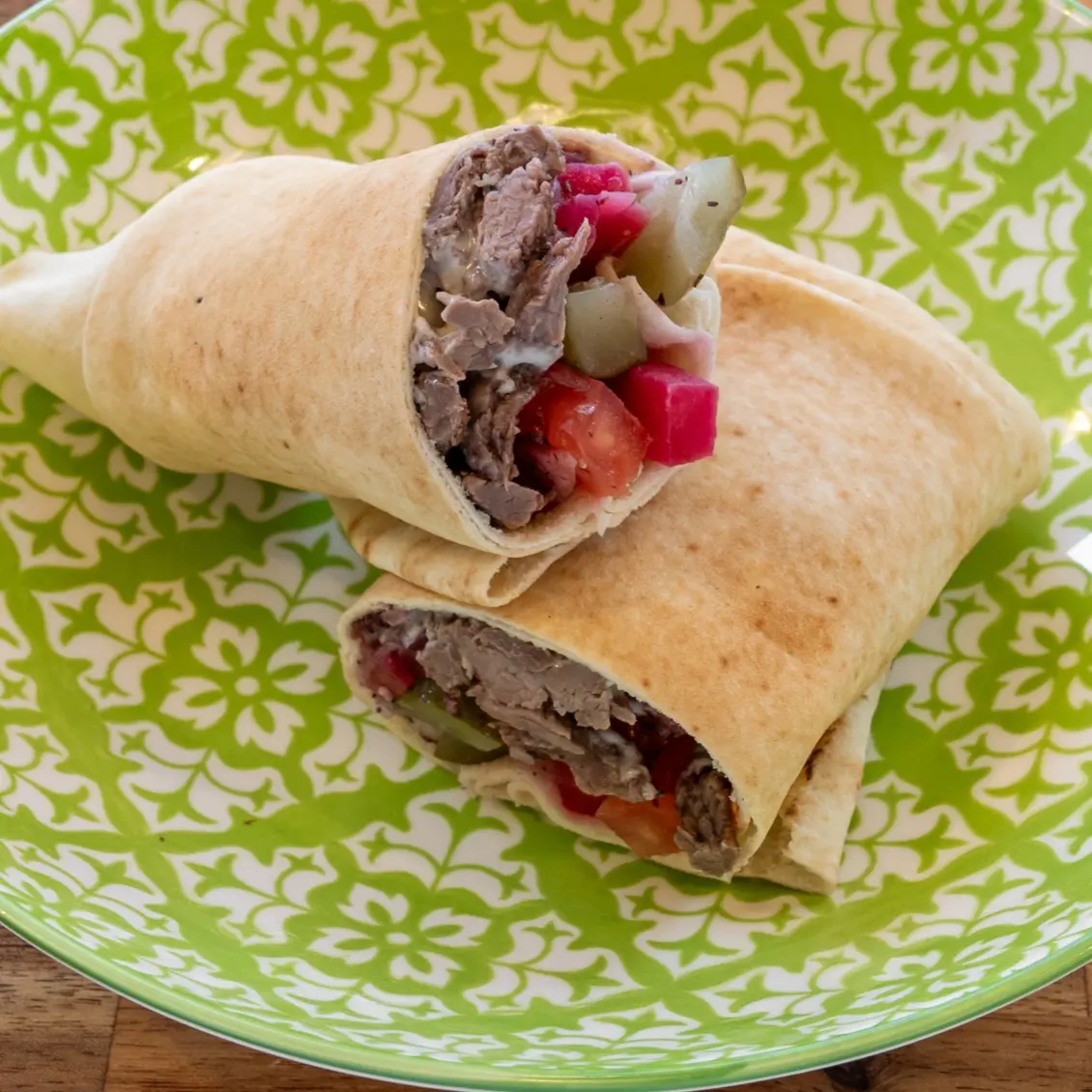 Sandwich libanais garni de bœuf, servi sur une assiette verte avec garniture visible
