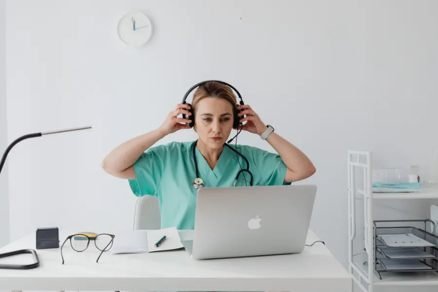 AI assistant for healthcare used by a nurse in green scrubs wearing a headset while looking attentively at her laptop.