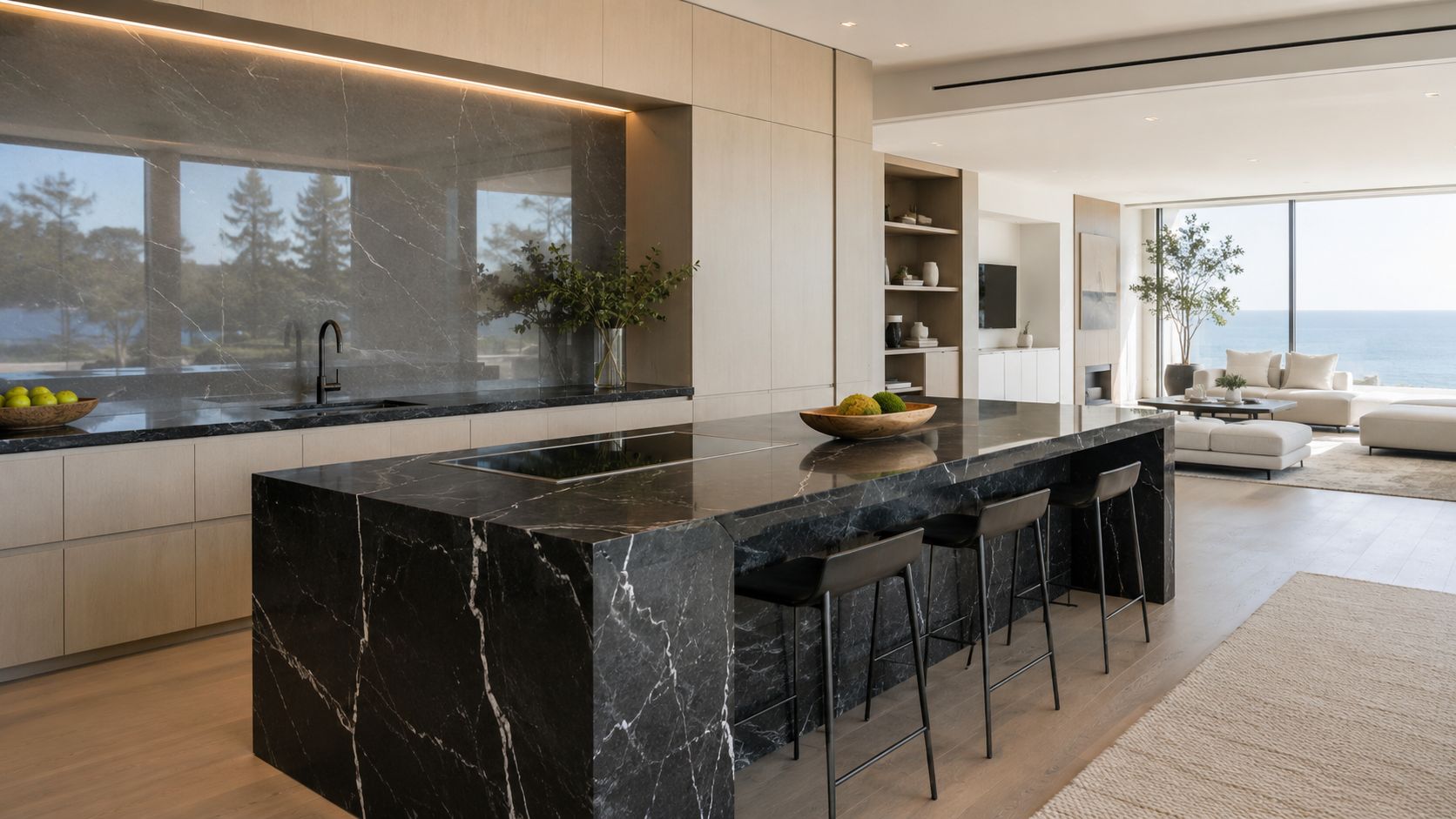 A luxurious modular kitchen featuring dark marble countertops, black bar stools, and minimalist light wood cabinetry.