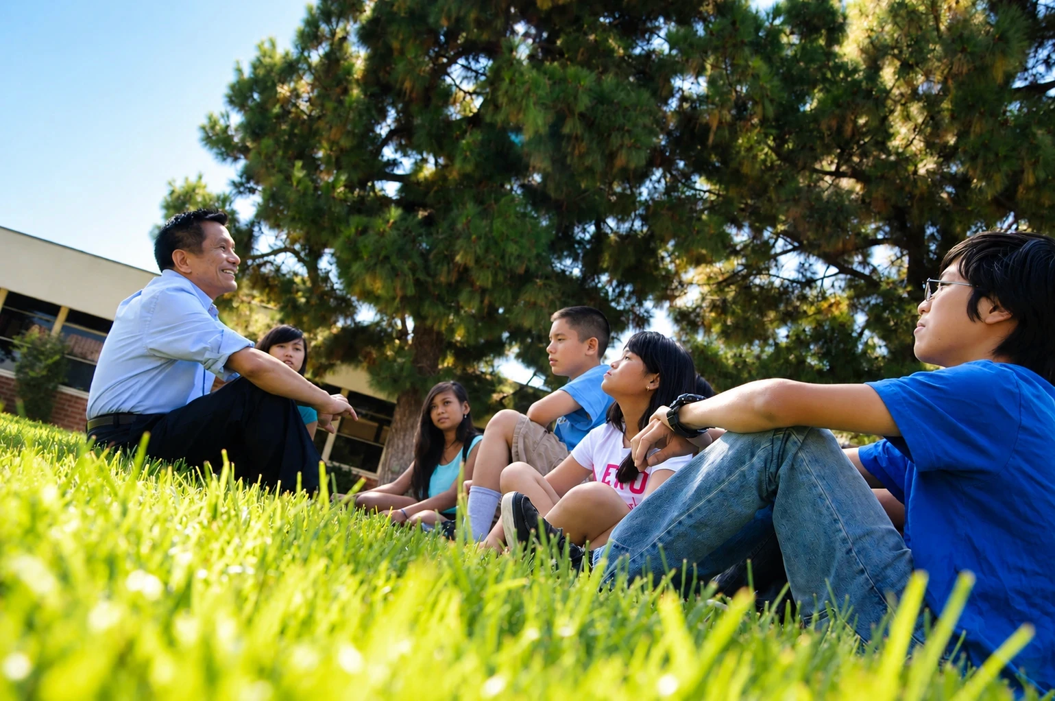 Phát Bùi ngồi trên bãi cỏ cùng một nhóm học sinh Garden Grove và trò chuyện với các em
