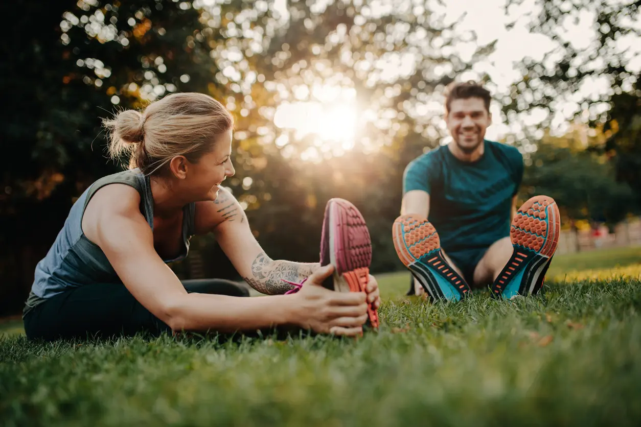 Two people stretching together outdoors in a park representing interpersonal connection and team wellbeing
